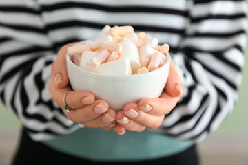 Young woman holding bowl with tasty marshmallows, closeup