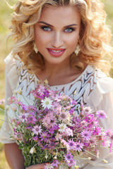 Naklejka premium Curly blonde in a park with a bouquet of field violet flowers..