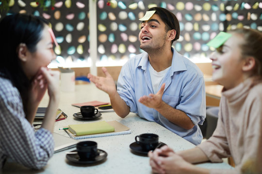 Group of cheerful friendly teenagers playing name game while relaxing in college cafe