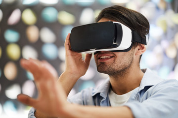 Young happy man in vr goggle enjoying virtual travel and touching new three dimension reality