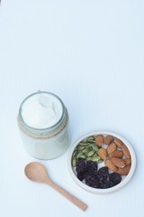 Plain yoghurt in white bowl, honey, cereal, raisin and wood spoon on white wooden table background