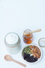 Fototapeta premium Plain yoghurt in white bowl, honey, cereal, raisin and wood spoon on white wooden table background