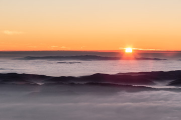 Fototapeta premium Beautiful sunset over a valley filled by fog with mountains and hills