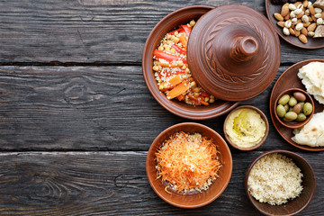 Moroccan traditional tajin and various snacks on dark wooden table. Carrot Salad, Couscous, Olives, Hummus. Flat lay