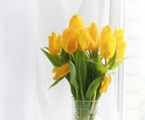 A bouquet of red tulips in a vase on the windowsill. A gift for a woman's day from red tulip flowers. Beautiful red flowers in a vase by window.