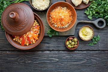 Moroccan traditional tajin and various snacks on dark wooden table. Carrot Salad, Couscous, Olives, Hummus. Flat lay