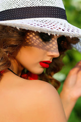 Beautiful curly girl in a white hat and a black swimsuit posing against the park background