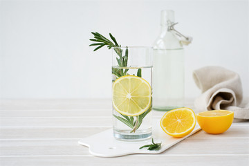 Glass of water with lemon and rosemary on light background