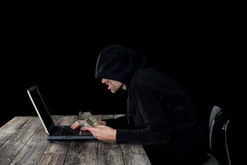 hacker in black hoody with laptop and dollar notes