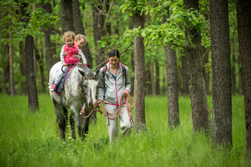 Obraz premium Girl having fun with mother and horse in the woods, young pretty girl with blond curly hair, freedom, joy, movement, outdoor, spring, healthy, happy family, cheerfull, kid on vacation