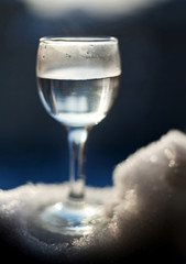 Glass wineglass with liquid standing on the snow with a blurred background