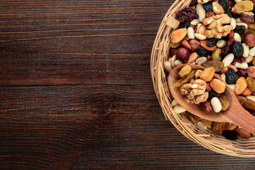 Dried fruits and nuts on a wooden background in a wicker basket with a wooden spoon