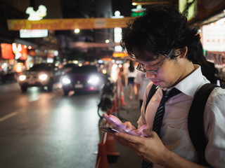 Young Asian business man using mobile smart phone in the street at night. Social and internet of thing concept.