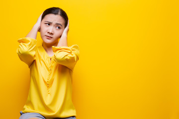 Woman covering her ears and standing isolated over yellow background