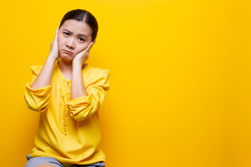 Woman covering her ears and standing isolated over yellow background