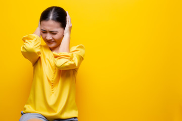 Woman covering her ears and standing isolated over yellow background