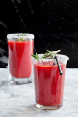 Tomato juice garnished with a rosemary branch on a marble background