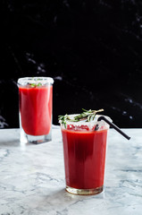 Tomato juice garnished with a rosemary branch on a marble background