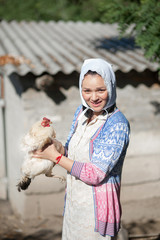 A woman in a village is holding a hen. Shooting in retro style.