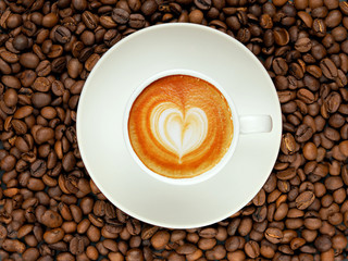 Coffee beans as background and white cup with coffee on a white saucer