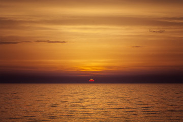 Naklejka na ściany i meble Beautiful sea orange sunset with sun on the horizon and cloudy sky