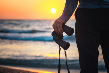 Close-up of binoculars in the hands of a man standing on the beach