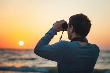 A man looking through binoculars standing on the beach