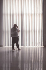 Lonely fat woman standing near the window