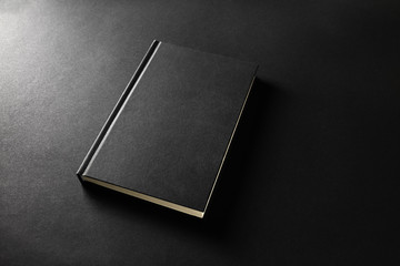 Mockup of closed blank black book on black paper background.