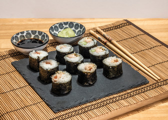 Sushi is a dish made from steamed white rice, rolled in gim with salmon and other ingredients with caviar and served in bite-size slices. Wasabi sauce in saucer.