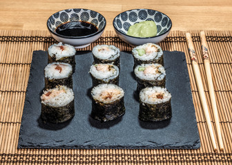 Sushi is a dish made from steamed white rice, rolled in gim with salmon and other ingredients with caviar and served in bite-size slices. Wasabi sauce in saucer.