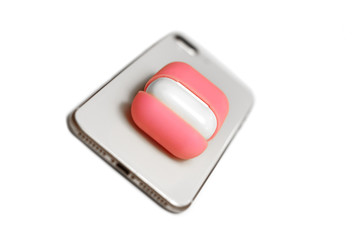 Little white earphones with charger box in bright pink cover box, mobile phone, chosen focus, dinamic expression. White background, copy space, close up.
