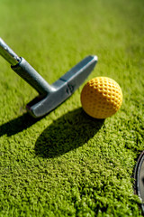 Mini Golf yellow ball with a bat near the hole at sunset