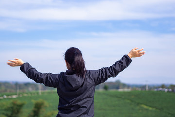 Back view of a woman standing and hands up at tea plantation.
