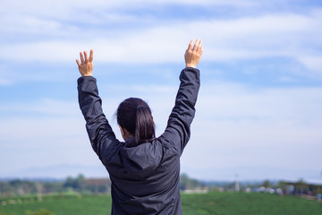 Back view of a woman standing and hands up at tea plantation.