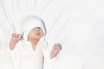 Curious little baby boy wearing white knitted hat and lying on white