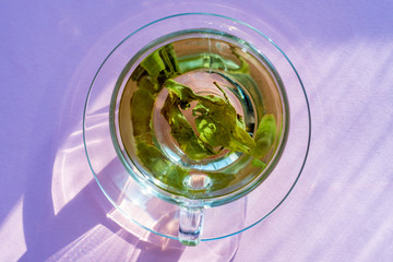 top view of transparent cup with green tea on purple background.