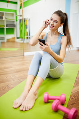 Full length portrait of pretty young woman  using smartphone during work out and smiling at camera