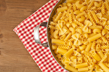 various uncooked raw pasta in a classical metal bowl with red dishtowel in rustic style