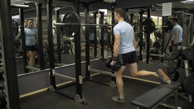 Attractive man doing lunges step-ups with heavy dumbbell.