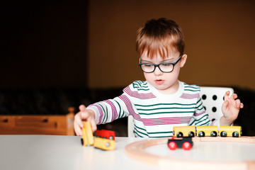 little boy with syndrome dawn in the black glasses playing with wooden railway