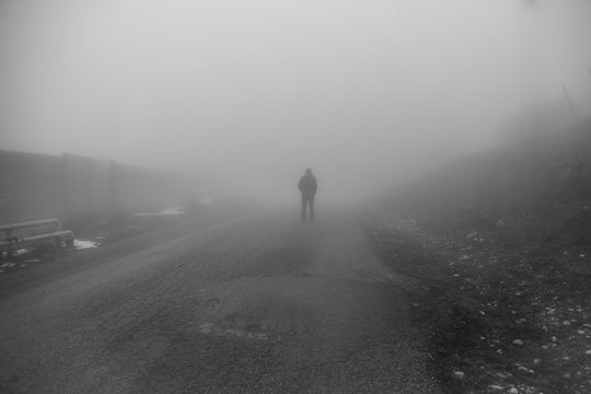 Man walking away on misty road. Man standing alone on rural foggy and misty asphalt road.