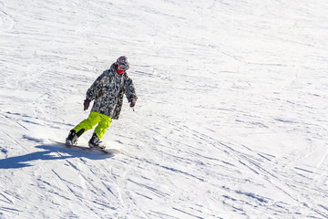 Snowboarder quickly rolls down the mountain on loose snow on a sunny day.