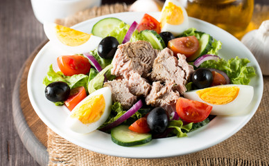 Fresh fish tuna salad made of tomato, ruccola, tuna, eggs, arugula, crackers and spices. Caesar salad in a white bowl on wooden background
