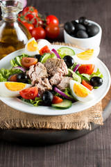 Fresh fish tuna salad made of tomato, ruccola, tuna, eggs, arugula, crackers and spices. Caesar salad in a white bowl on wooden background