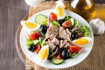 Fresh fish tuna salad made of tomato, ruccola, tuna, eggs, arugula, crackers and spices. Caesar salad in a white bowl on wooden background