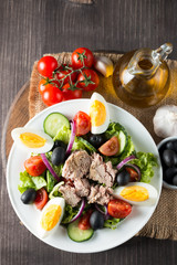 Fresh fish tuna salad made of tomato, ruccola, tuna, eggs, arugula, crackers and spices. Caesar salad in a white bowl on wooden background