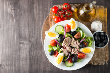 Fresh fish tuna salad made of tomato, ruccola, tuna, eggs, arugula, crackers and spices. Caesar salad in a white bowl on wooden background