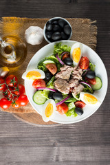 Fresh fish tuna salad made of tomato, ruccola, tuna, eggs, arugula, crackers and spices. Caesar salad in a white bowl on wooden background