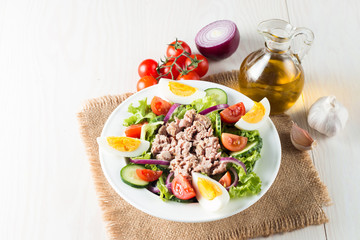 Fresh fish tuna salad made of tomato, ruccola, tuna, eggs, arugula, crackers and spices. Caesar salad in a white bowl on wooden background